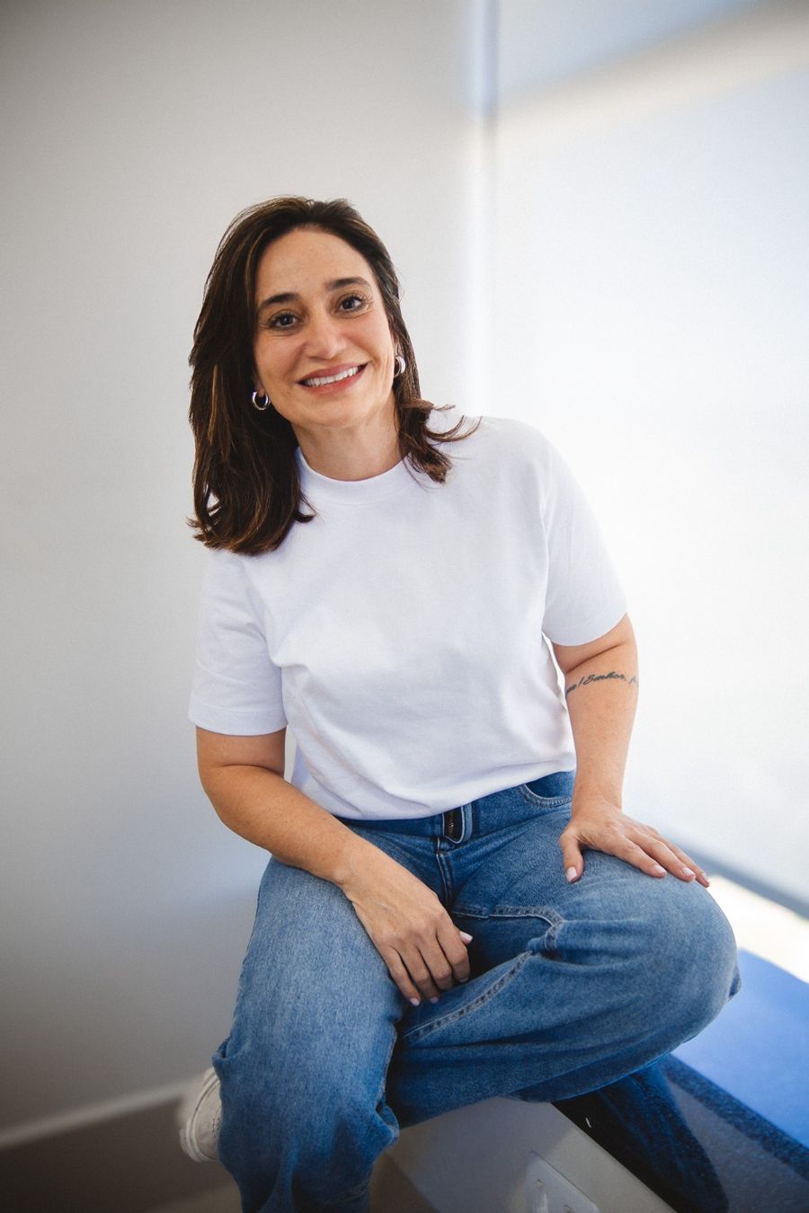 Raquel Pozo sorrindo, sentada em ambiente claro
